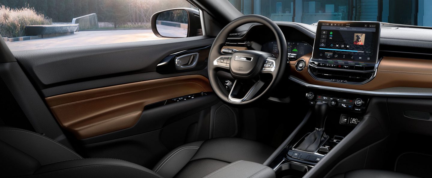 The front seat area in the 2025 Jeep Compass Limited, concentrating on the driver seat, steering wheel, Uconnect touchscreen and center console.