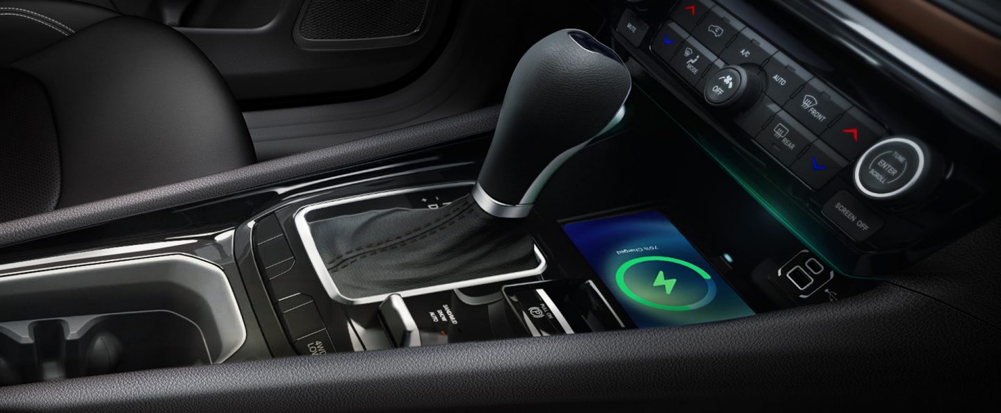 A close-up of the center console in the 2025 Jeep Compass Limited, including cup holders, the shifter, the wireless charging pad and climate controls.