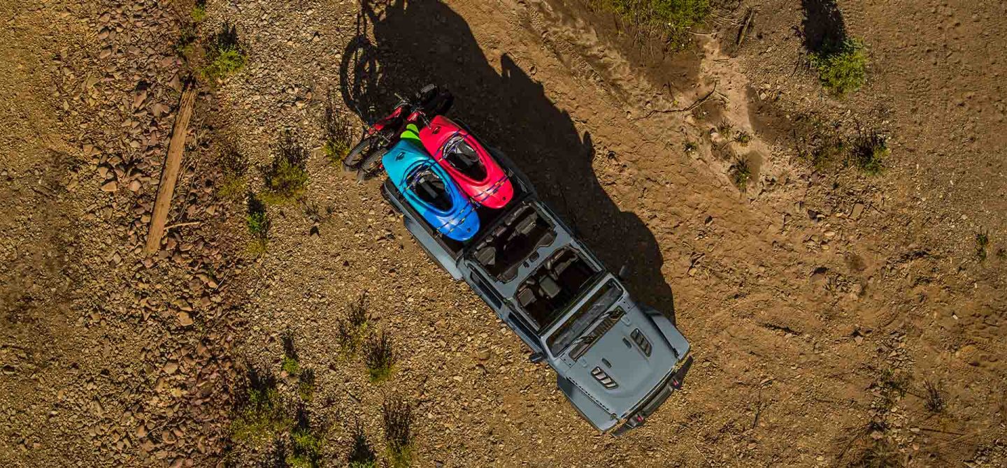 A top-down angle of a gray 2025 Jeep Gladiator Mojave X with its doors and roof removed, being driven in loose sand, creating heavy tracks as it goes.