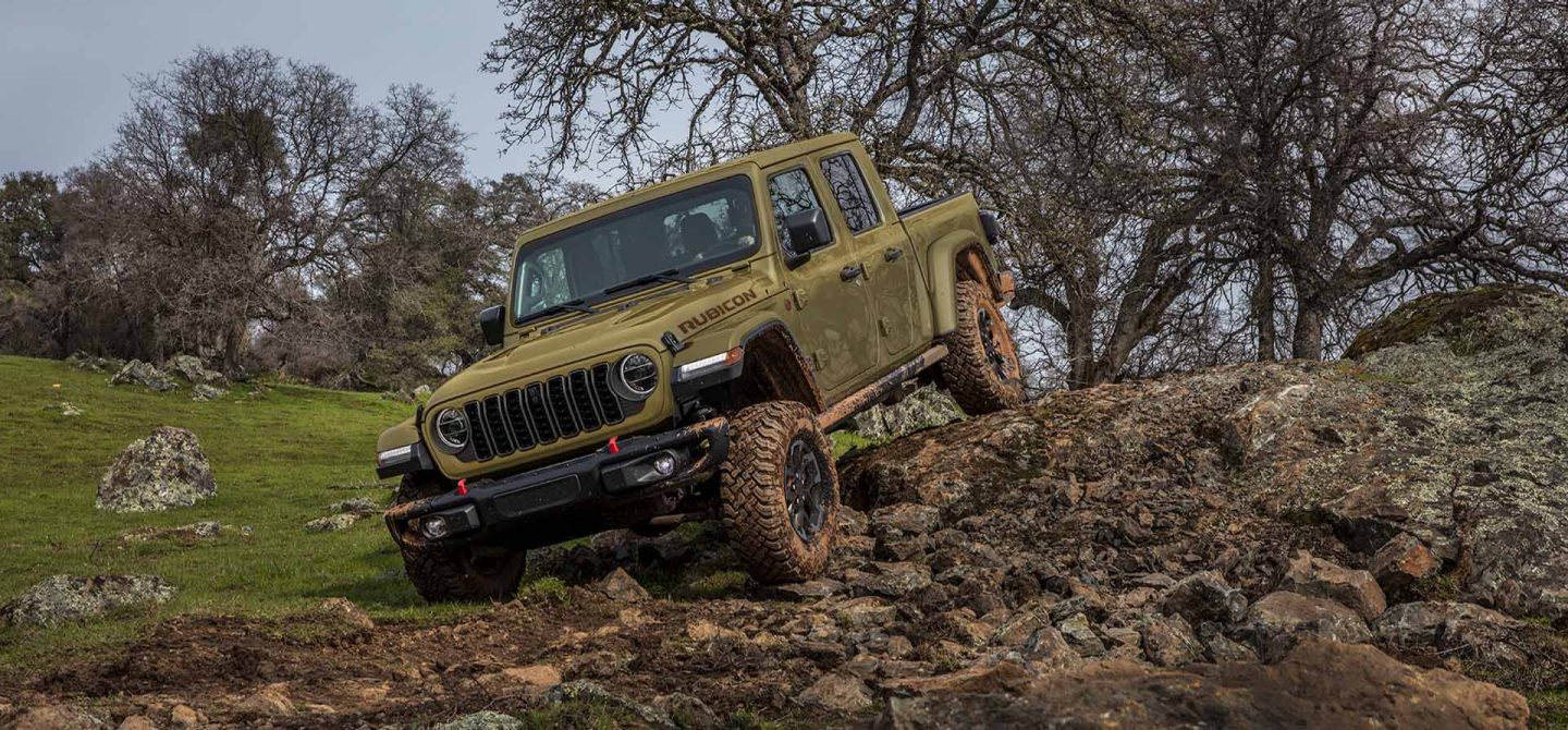 An olive green 2025 Jeep Gladiator Rubicon X descending a rugged, rocky trail off-road.