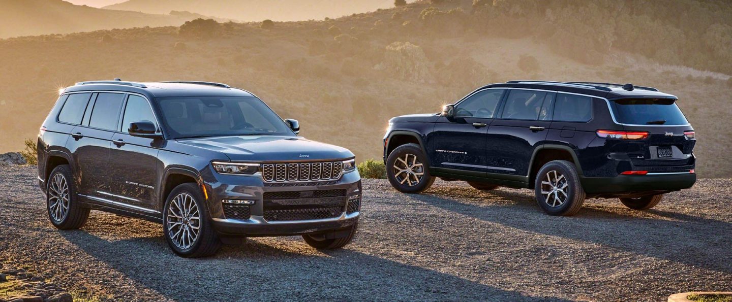 A gray 2025 Jeep Grand Cherokee Summit Reserve and a black Jeep Grand Cherokee Limited parked opposite of each other on a gravel mountain road at sunset.