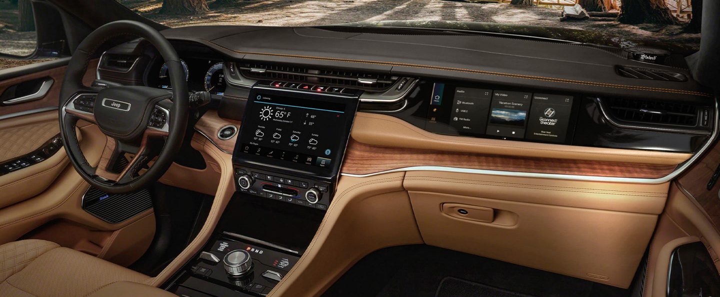 The steering wheel, Uconnect touchscreen, Front Passenger Interactive Touchscreen Display, center stack controls and center console in the 2025 Jeep Grand Cherokee Summit Reserve.