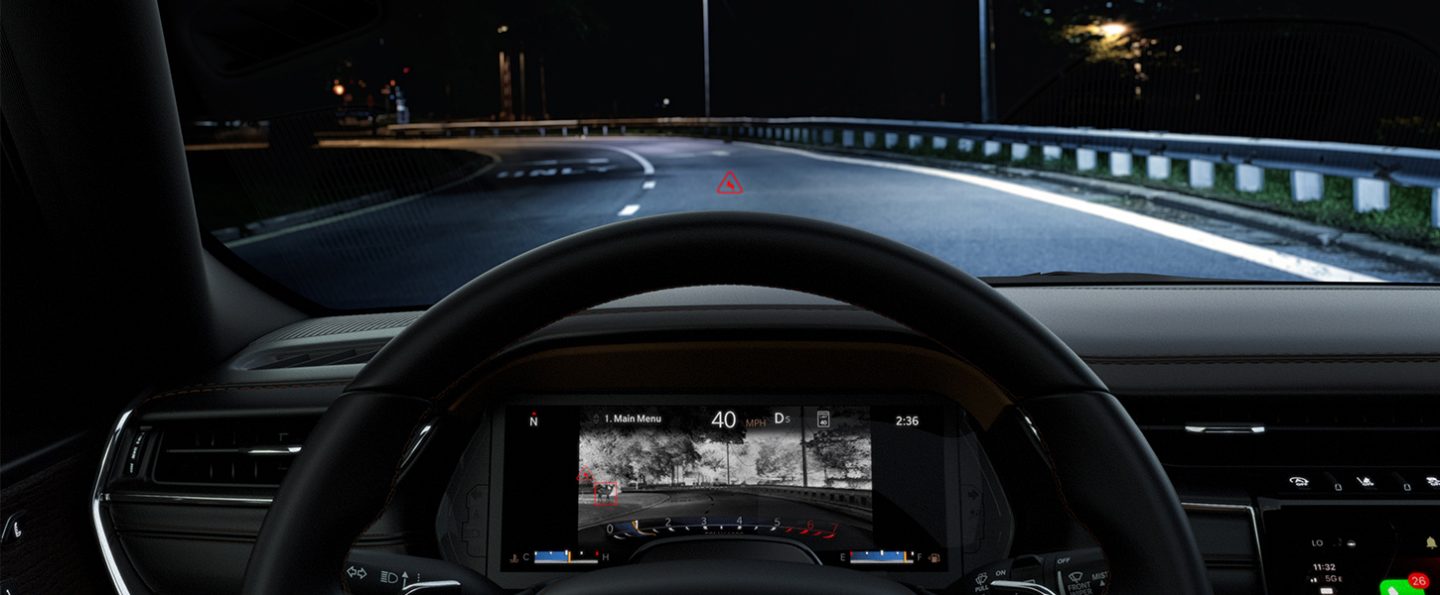 The Digital Cluster in the 2025 Jeep Grand Cherokee displaying a night vision camera image of the road ahead, revealing an animal in the left corner of the screen, while through the windshield the animal is not visible.