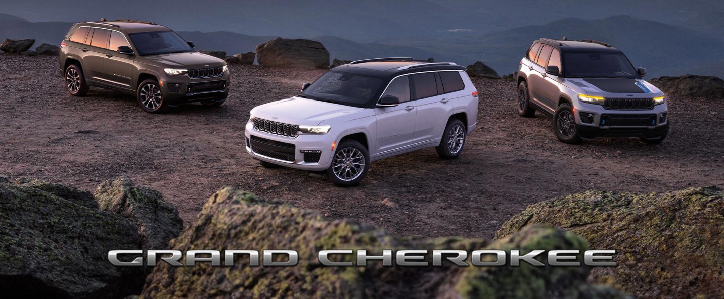 Three 2025 Jeep Grand Cherokee models parked on a rocky clearing at dusk, with mountains in the background; from left to right: a gray Grand Cherokee Overland, white Grand Cherokee Summit and silver Grand Cherokee Trailhawk 4xe with black hood insert. Grand Cherokee.