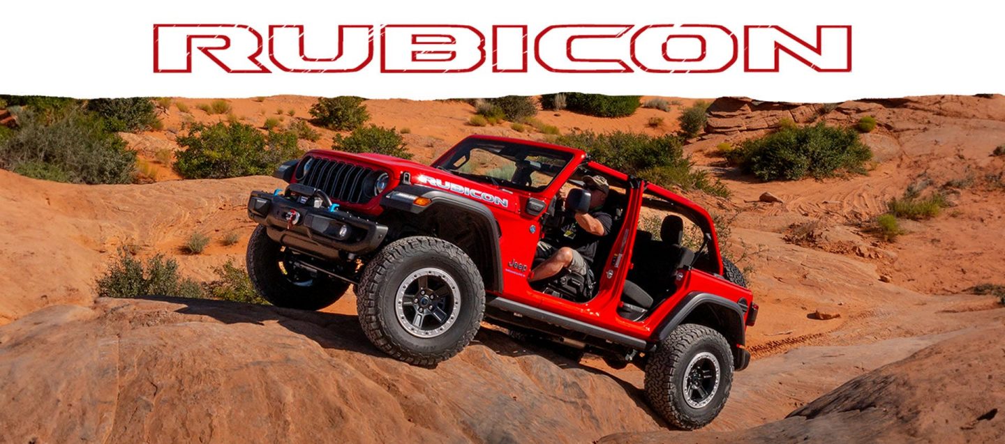 A red 2025 Jeep Wrangler Rubicon 4xe with its doors and roof removed, ascending a sandy hill in the desert.