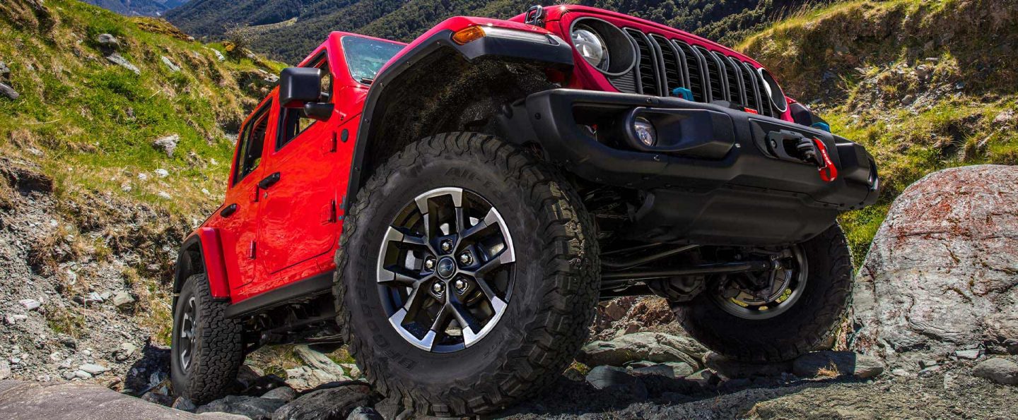 A low-lying angle of the wheels, tires and undercarriage of the 2025 Jeep Wrangler Rubicon X 4xe climbing a rocky trail off-road.