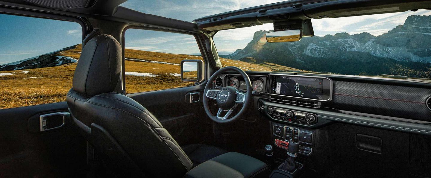 The front row in the 2025 Jeep Wrangler focusing on the open sunroof, steering wheel, Uconnect touchscreen and dash.