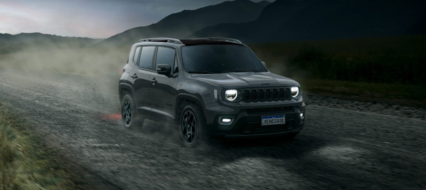 A view of the 2025 Jeep Renegade being driven on a rural road, with its headlamps on.